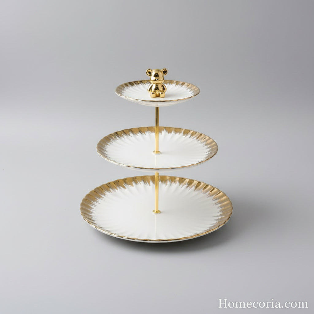 Three-tiered plate with gold rim and bear figurine on a white surface with a branded box in the background.