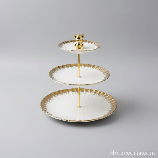 Three-tiered plate with gold rim and bear figurine on a white surface with a branded box in the background.